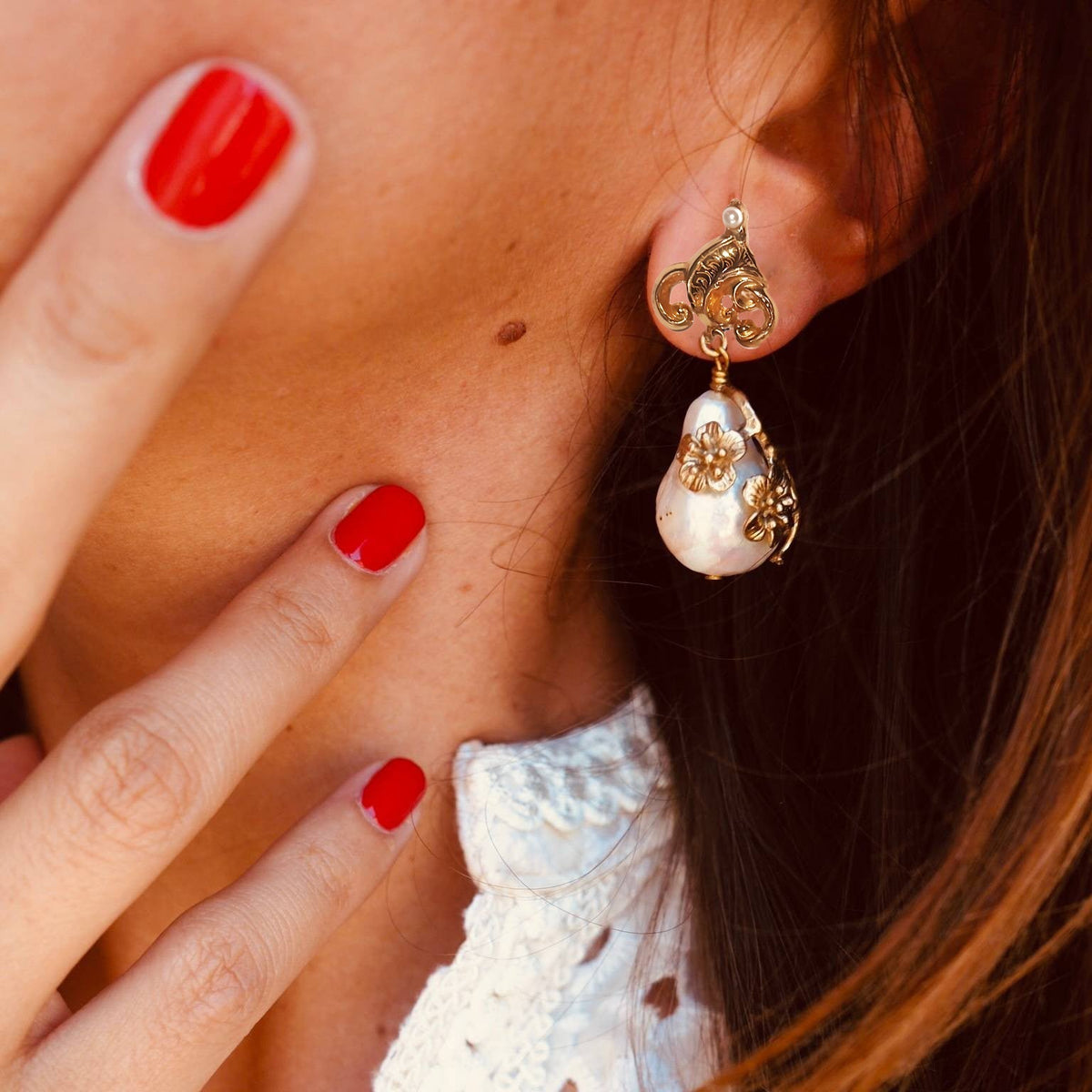 Boucle d’oreille Perle Baroque dorée My Little Vendôme portée : perle blanche de forme irrégulière, ongles rouges, col de dentelle