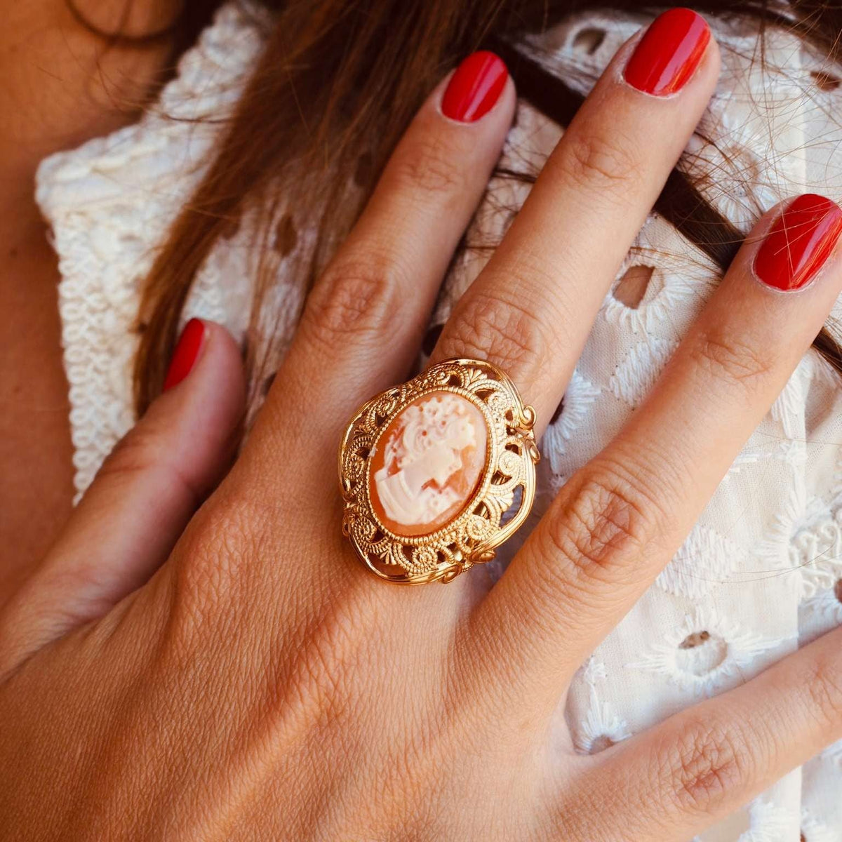 Bague Camée Louvre My Little Vendôme en gros plan : camée orangé à profil blanc, monture dorée ajourée, vernis rouge