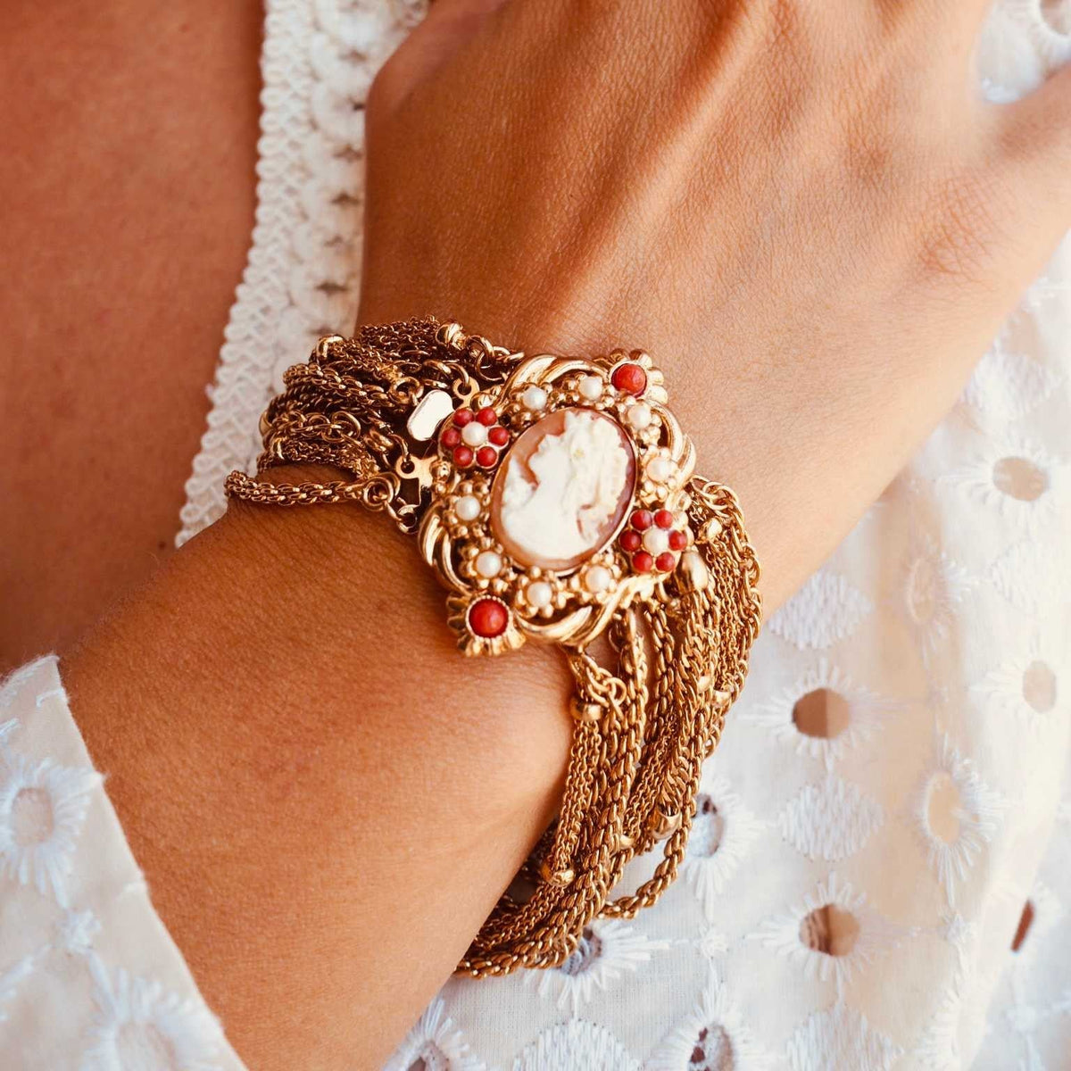 Bracelet Camée Louvre My Little Vendôme au poignet : médaillon à camée orangé, perles blanches, billes rouges, chaînes dorées