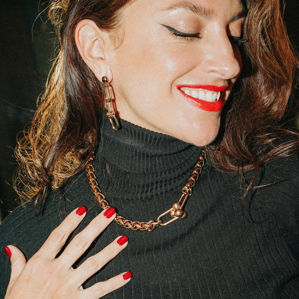 Femme souriante, yeux fermés, en col roulé noir, collier Mabillon doré et boucle d’oreille Arc My Little Vendôme