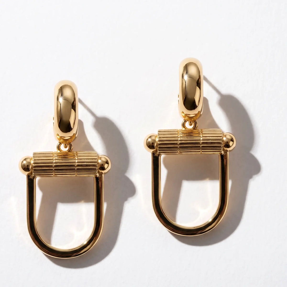 Paire de boucles Montorgueil dorées sur fond blanc, avec leurs ombres.