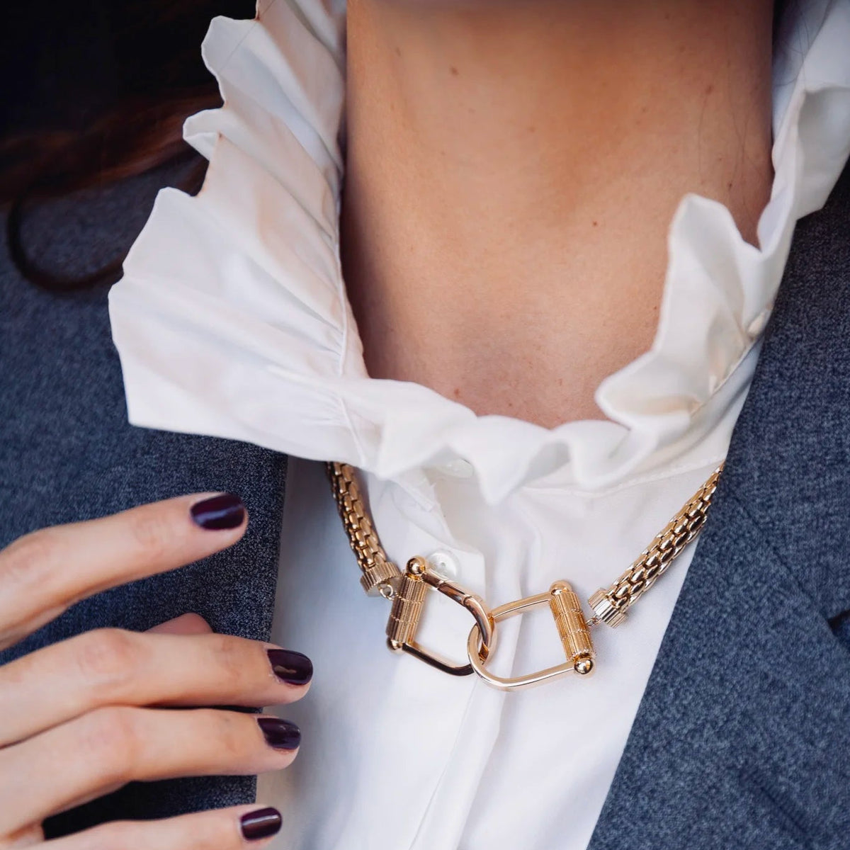 Collier Montorgueil au creux du cou, sur un col blanc à volants et un blazer gris.